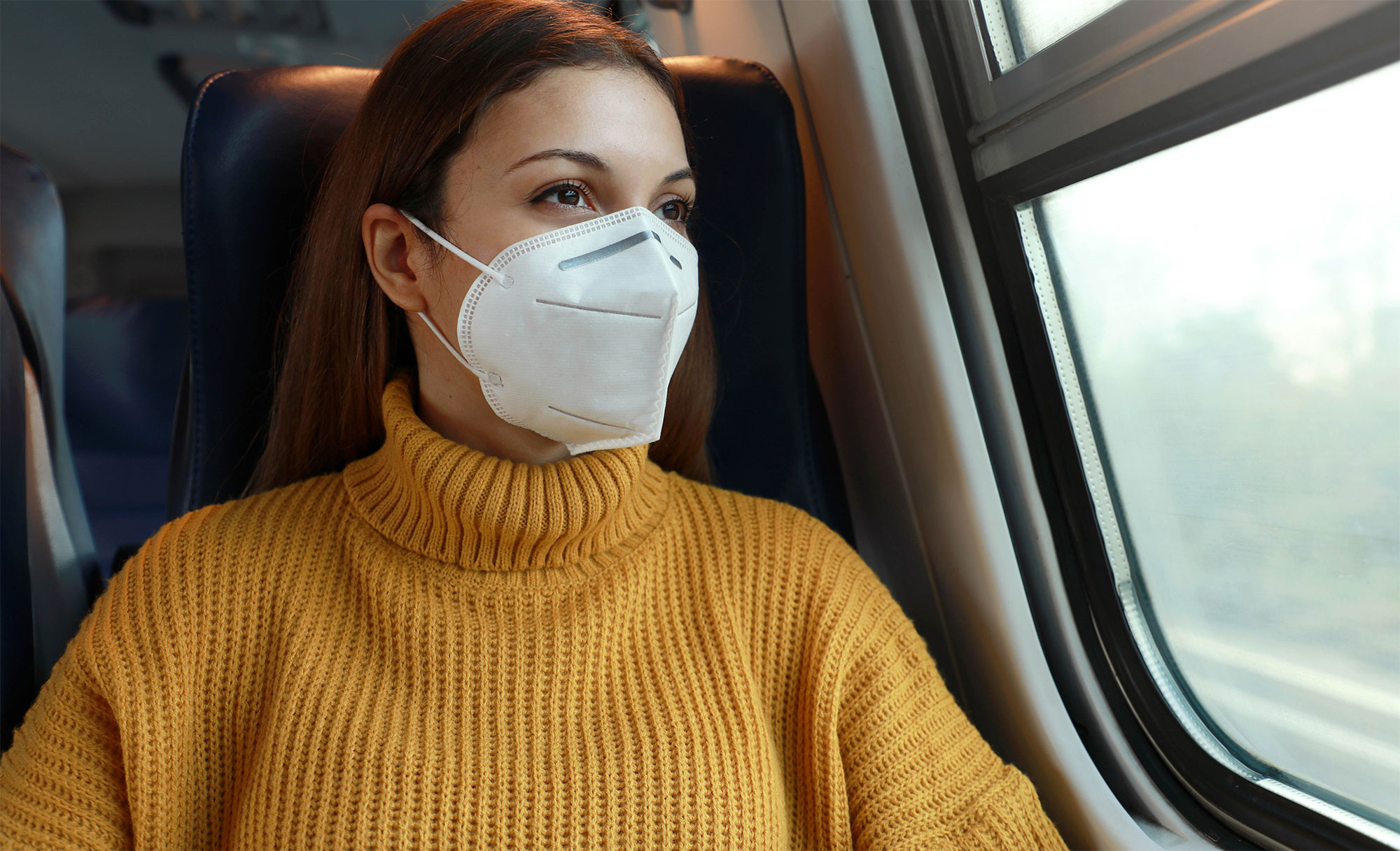 Frau sitzt mit FFP2-Maske im Zug