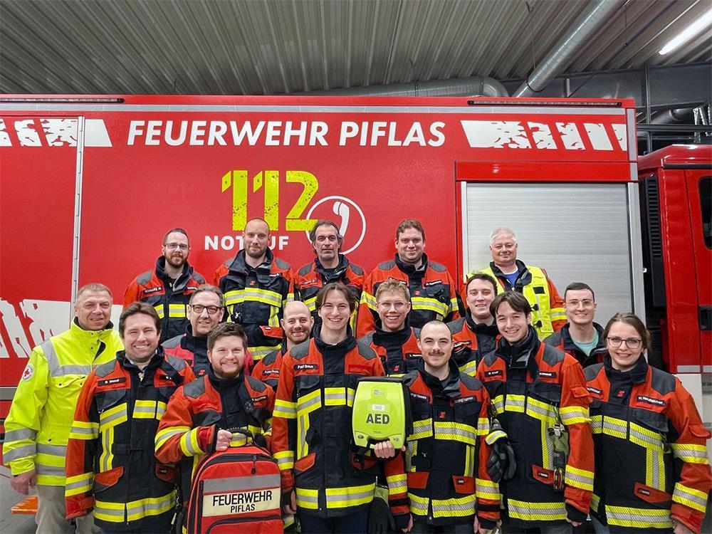 Gruppenaufnahme einer Feuerwehrmannschaft vor ihrem Einsatzwagen