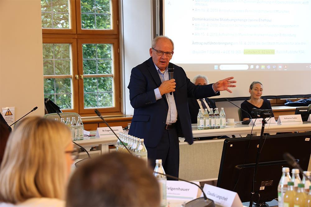 Obdachlosigkeit-in-Kommunen Besprechung: Mann steht mit Mikrofon vor einer Leinwand