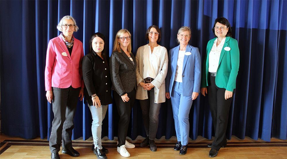 Sechs Frauen stehen vor einem blauen Vorhang