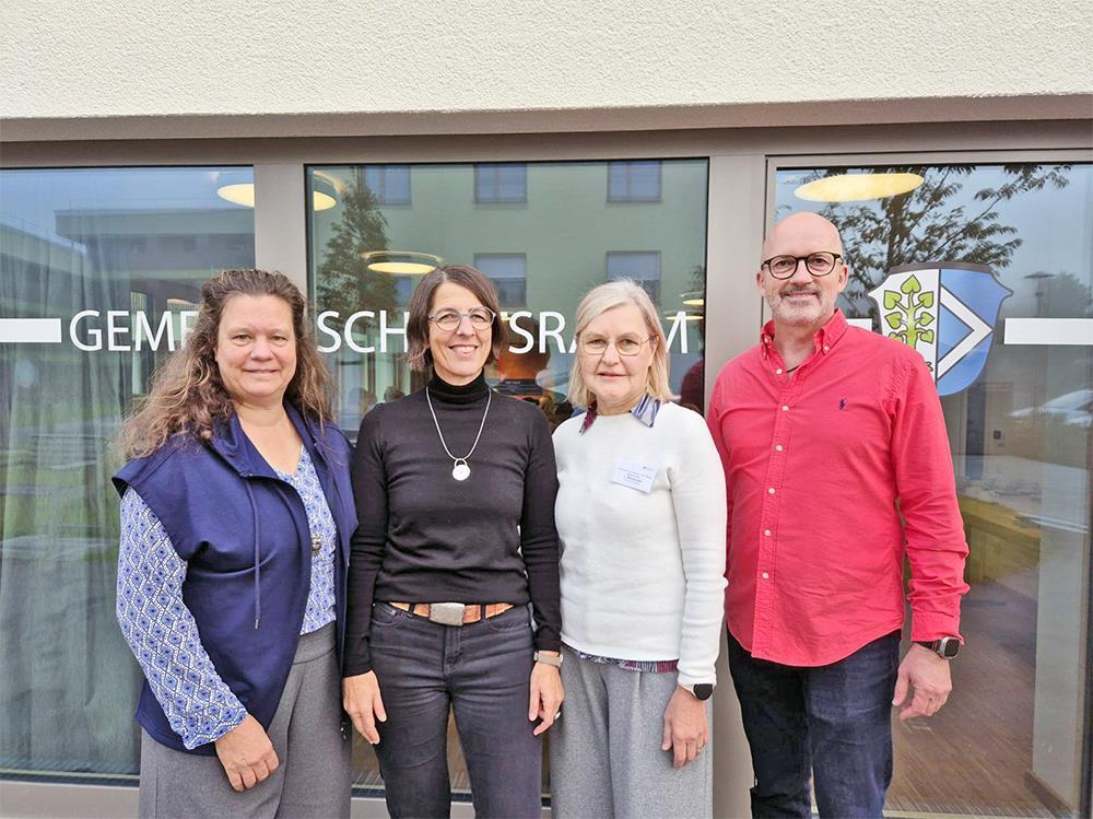 Drei Frauen und ein Mann stehen vor einer Glastür