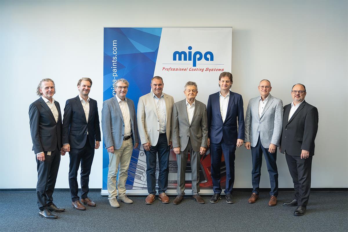 Acht Personen vor einer einem Werbebanner der Firma mipa 